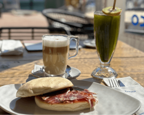 Breakfast muffin on a plate next to a coffee and a juice